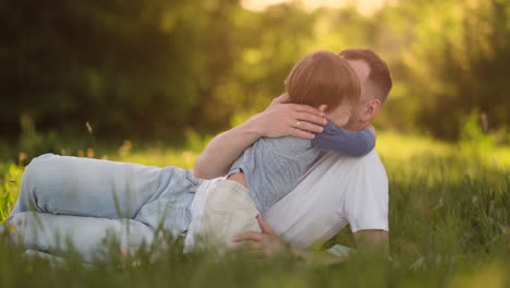 Dad-and-son-hugging-lying-in-the-meadow-at-sunset.